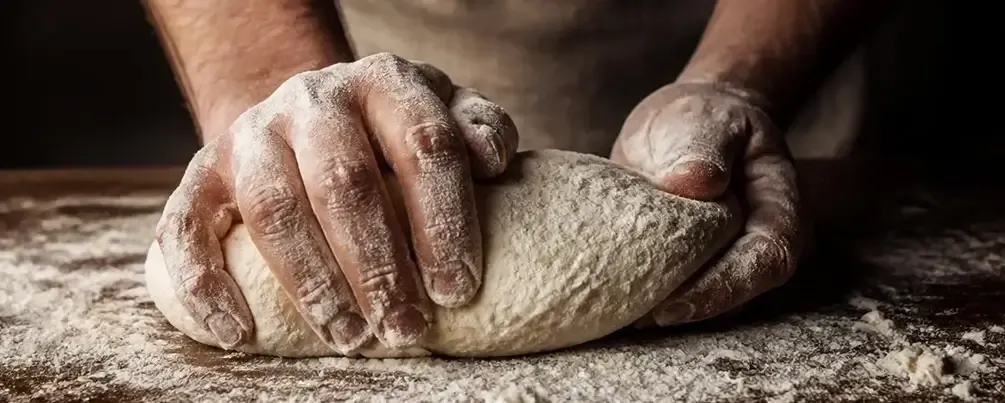 Manos artesanas enharinadas amasando pan en el obrador de Bliss Soul Bakery