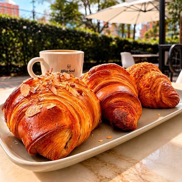 Croissants artesanales de masa laminada servidos en bandeja junto a taza de café Bliss Soul